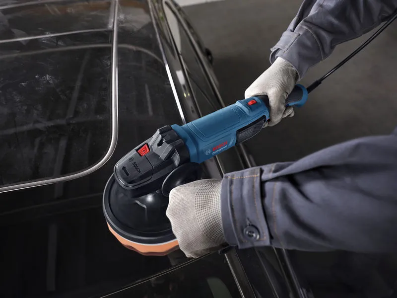 Seseorang yang mengenakan perlengkapan keselamatan memoles atap mobil dengan alat poles bertenaga.