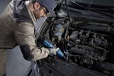 Seseorang yang mengenakan perlengkapan keselamatan menggunakan kunci pas ratchet tanpa kabel untuk memperbaiki mesin mobil.