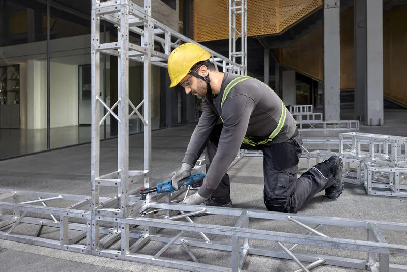 Seseorang yang mengenakan peralatan keselamatan mengencangkan baut pada rangka logam dengan kunci ratchet tanpa kabel.