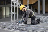 Seseorang yang mengenakan peralatan keselamatan mengencangkan baut pada rangka logam dengan kunci ratchet tanpa kabel.