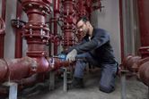 Seseorang yang mengenakan peralatan keselamatan menggunakan kunci pas ratchet tanpa kabel pada sistem pipa merah.