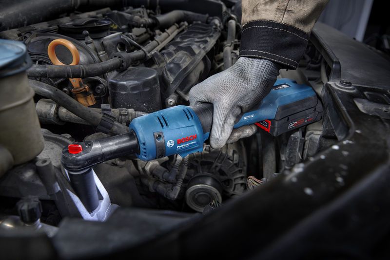 Seseorang yang mengenakan perlengkapan keselamatan menggunakan kunci ratchet tanpa kabel untuk mengencangkan baut di mesin mobil.