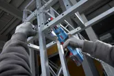 Seseorang yang mengenakan peralatan keselamatan mengencangkan baut pada rangka logam menggunakan kunci ratchet tanpa kabel.