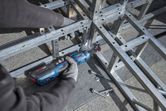 Orang yang mengenakan peralatan keselamatan mengencangkan baut pada rangka logam menggunakan kunci ratchet tanpa kabel.