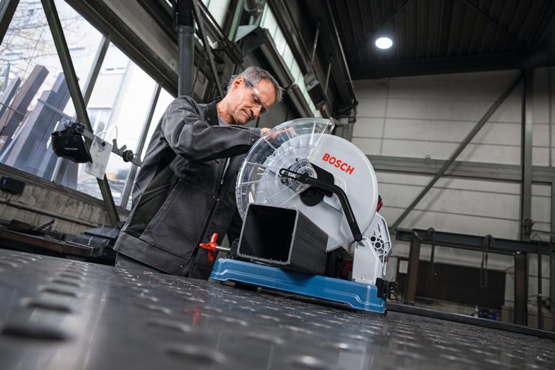 Seseorang yang mengenakan peralatan keselamatan menyiapkan gergaji pemotong logam untuk memotong pipa logam.