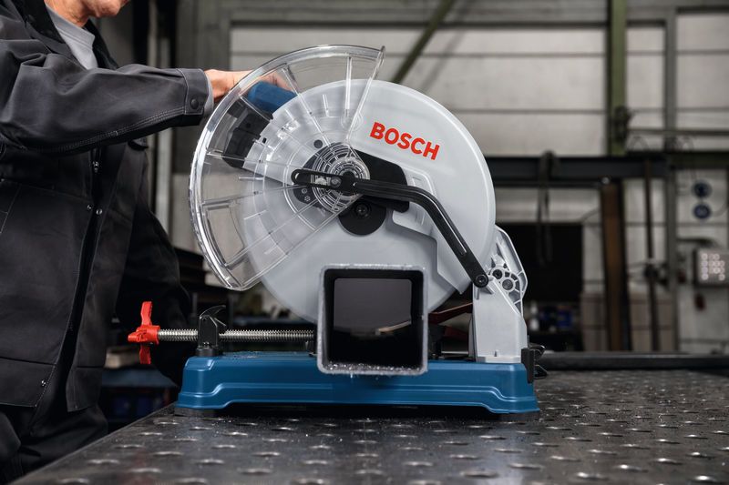 Seseorang yang mengenakan peralatan keselamatan mengoperasikan gergaji pemotong logam pada pipa baja.