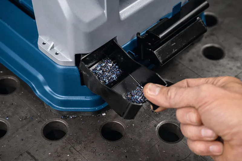 Seseorang mengosongkan baki serpihan logam dari gergaji pemotong logam di meja kerja.