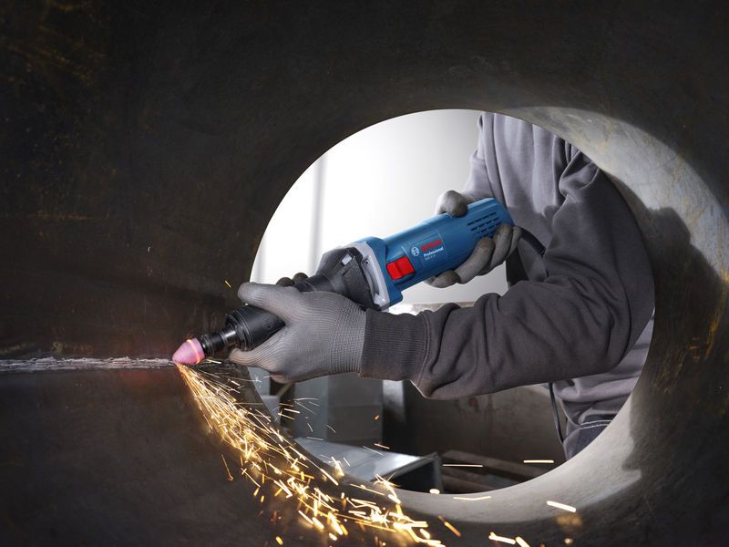 Seseorang yang mengenakan perlengkapan keselamatan menggunakan penggiling lurus untuk menghaluskan bagian dalam pipa logam.