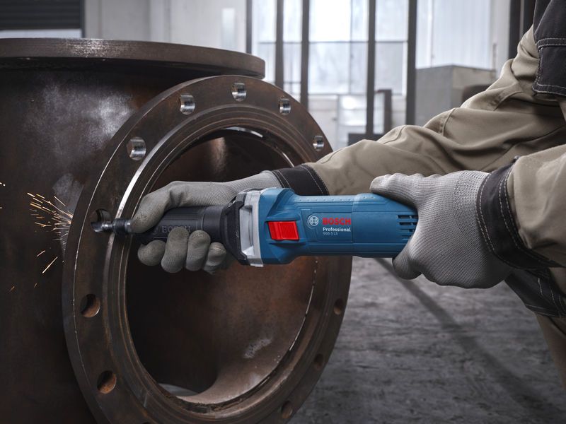 Seseorang yang mengenakan peralatan keselamatan menggiling pipa logam dengan penggiling lurus.