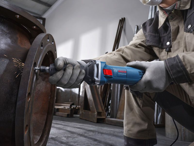 Seseorang yang mengenakan perlengkapan keselamatan menggunakan penggiling lurus untuk menggiling bagian dalam pipa logam besar.