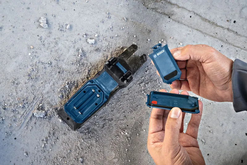 Seseorang mengganti baterai pada tempat perkakas listrik di lantai beton yang berdebu.