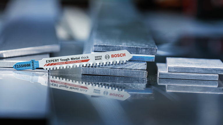 Mata gergaji ukir diletakkan pada tumpukan lembaran logam pada permukaan yang reflektif.