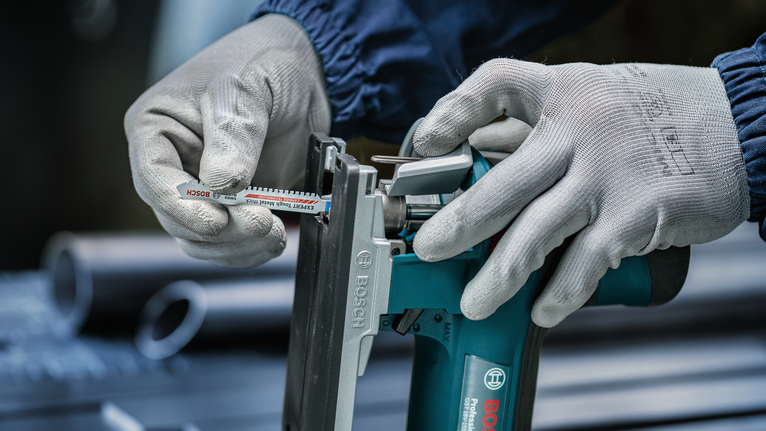 Orang yang mengenakan peralatan keselamatan memasukkan mata gergaji ke dalam perkakas listrik.