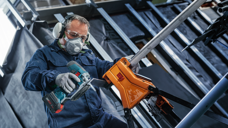 Seseorang yang mengenakan peralatan keselamatan memotong pipa logam dengan alat listrik tanpa kabel.