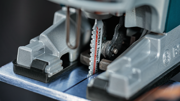 Tampilan dekat mata gergaji ukir yang memotong lembaran logam.