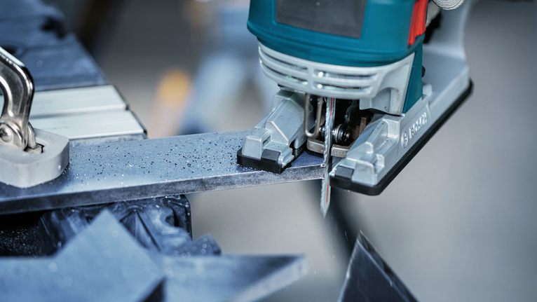 Gergaji ukir memotong batang logam di bengkel.