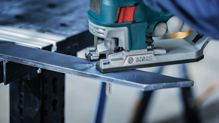 Orang yang mengenakan peralatan keselamatan memotong pelat logam dengan gergaji ukir.