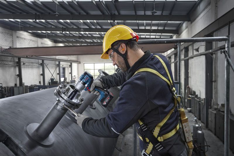 Seseorang yang mengenakan perlengkapan keselamatan menggunakan kunci pas benturan untuk mengencangkan baut pada tangki logam besar.