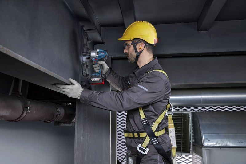 Seseorang yang mengenakan peralatan keselamatan mengencangkan baut pada balok baja menggunakan kunci pas benturan tanpa kabel.