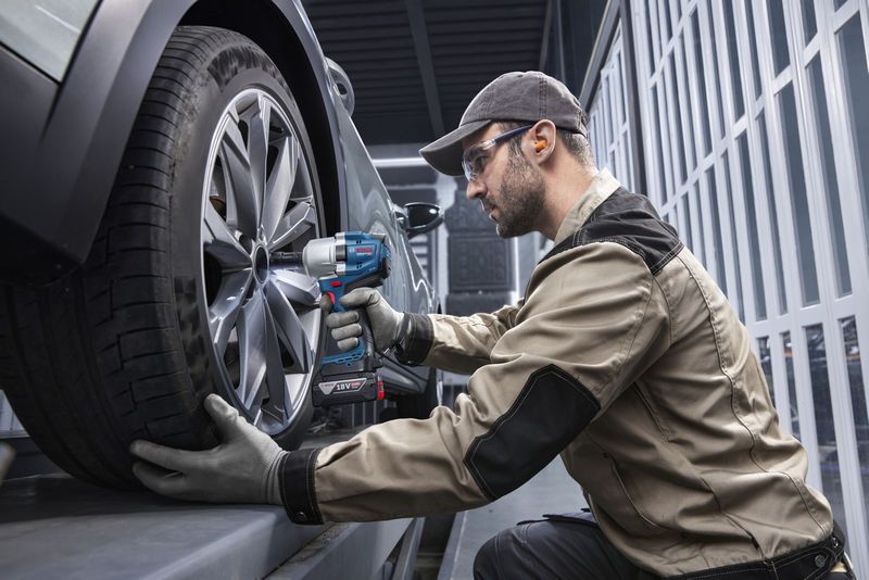 Seseorang yang mengenakan perlengkapan keselamatan menggunakan kunci pas benturan tanpa kabel untuk mengencangkan roda mobil.