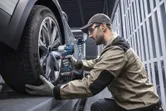 Seseorang yang mengenakan perlengkapan keselamatan menggunakan kunci pas benturan tanpa kabel untuk mengencangkan roda mobil.