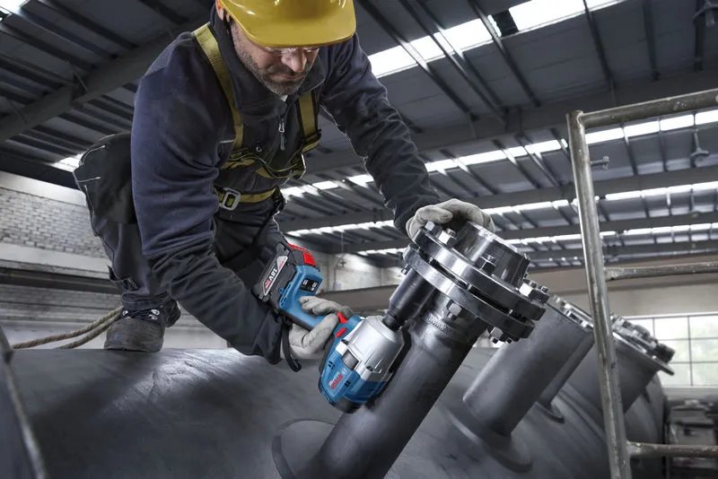 Seseorang yang mengenakan perlengkapan keselamatan menggunakan kunci pas benturan tanpa kabel pada pipa industri.