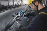Seseorang yang mengenakan peralatan keselamatan mengencangkan baut pada pipa industri dengan kunci pas benturan tanpa kabel.