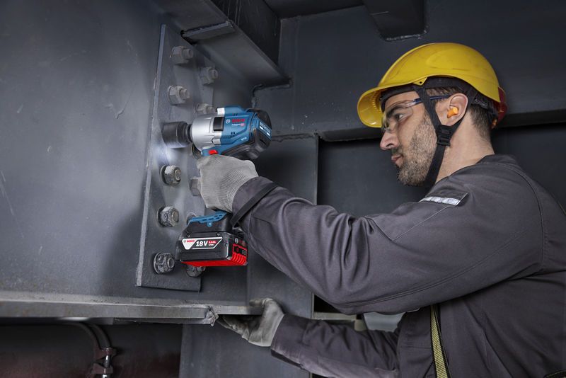 Seseorang yang mengenakan peralatan keselamatan mengencangkan baut pada balok baja menggunakan kunci pas benturan tanpa kabel.