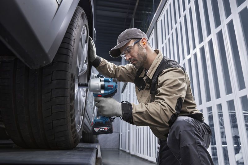 Seseorang yang mengenakan perlengkapan keselamatan menggunakan kunci pas benturan tanpa kabel pada roda mobil.