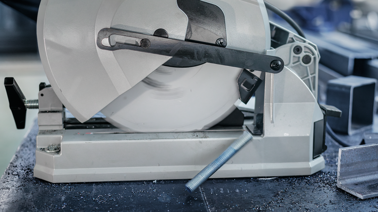 Gergaji pemotong logam mengiris batang baja di bengkel.