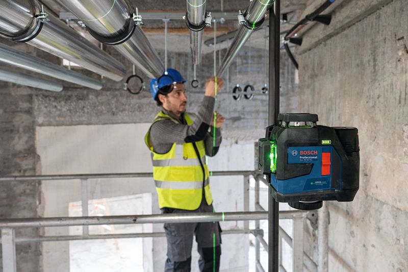 Seseorang yang mengenakan perlengkapan keselamatan menyelaraskan pipa menggunakan alat perataan laser.