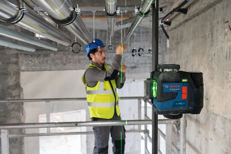 Seseorang yang mengenakan perlengkapan keselamatan menyelaraskan pipa menggunakan alat perataan laser.