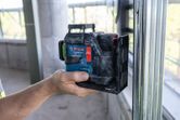 Seseorang memegang alat perata laser pada tiang logam di area konstruksi.