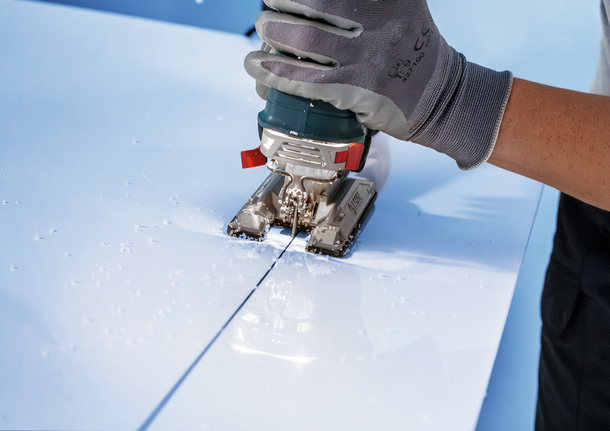 Pekerja yang mengenakan peralatan keselamatan menggunakan gergaji ukir untuk memotong garis lurus pada panel putih.