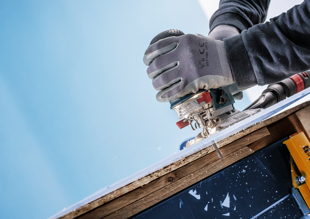 Pekerja yang mengenakan perlengkapan keselamatan menggunakan gergaji ukir untuk memotong sepotong kayu laminasi.