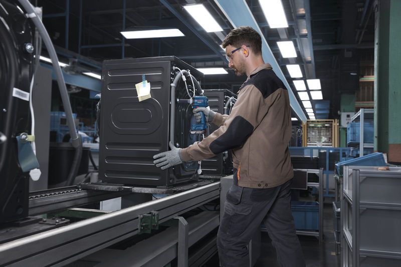 Seseorang yang mengenakan perlengkapan keselamatan mengencangkan suatu peralatan pada jalur perakitan menggunakan perkakas listrik.