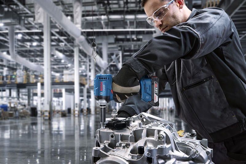 Seseorang yang mengenakan peralatan keselamatan menggunakan bor tanpa kabel pada bagian mesin.