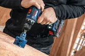Seseorang mengebor lubang besar ke dalam kayu menggunakan perkakas listrik di bengkel.