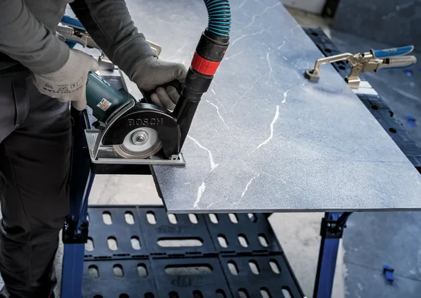 Orang yang mengenakan peralatan keselamatan memotong lempengan batu dengan gergaji listrik.