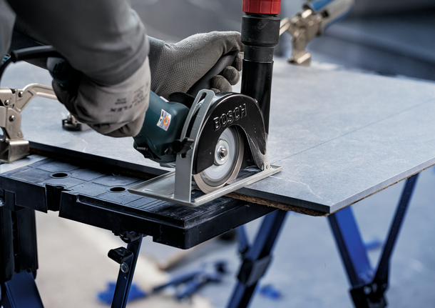 Orang yang mengenakan peralatan keselamatan memotong lembaran ubin dengan gergaji bundar.