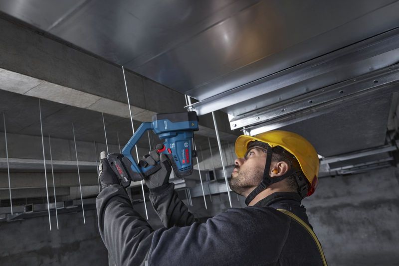 Seseorang yang mengenakan peralatan keselamatan menggunakan pemotong batang ulir tanpa kabel pada batang langit-langit.