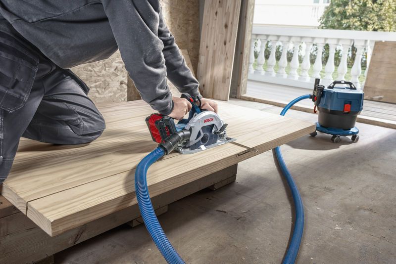 Seseorang memotong kayu dengan gergaji bundar tanpa kabel yang terhubung ke penyedot debu.