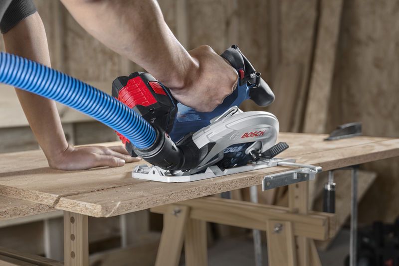 Seseorang memandu gergaji bundar tanpa kabel dengan selang penyedot debu sambil memotong kayu lapis.