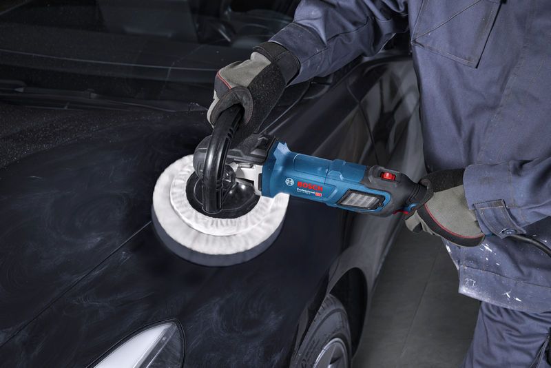 Seseorang yang mengenakan perlengkapan keselamatan menggunakan alat poles pada kap mobil berwarna hitam.