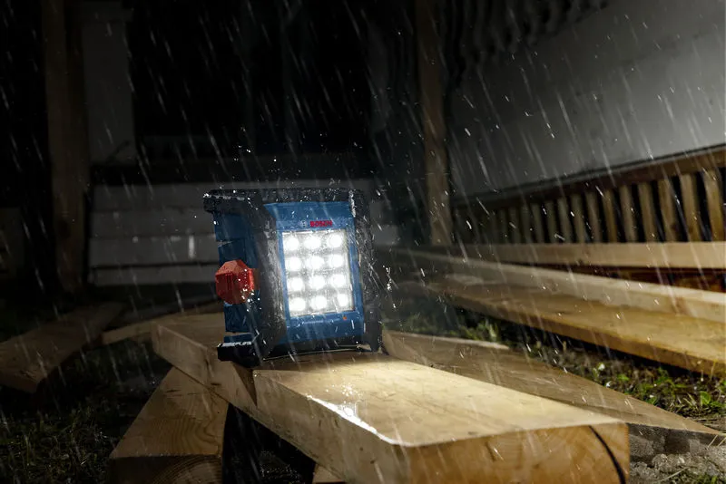 Lampu lokasi kerja tanpa kabel menerangi papan kayu di tengah hujan deras di lokasi konstruksi.