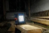Lampu lokasi kerja tanpa kabel menerangi papan kayu di tengah hujan deras di lokasi konstruksi.