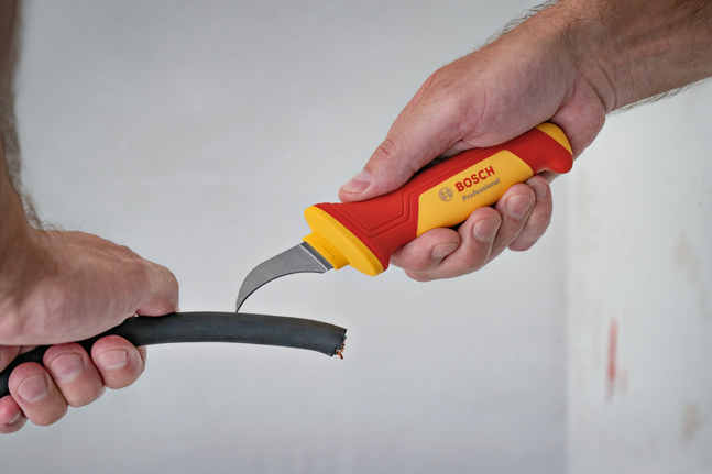 Seseorang menggunakan pisau berinsulasi untuk mengupas lapisan luar kabel tebal.