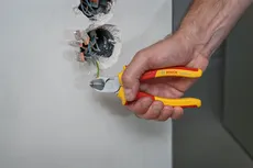 Seseorang memotong kabel listrik dengan tang berinsulasi di dekat stopkontak dinding.