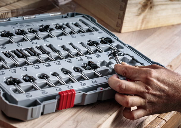 Seseorang memilih mata bor dari set yang tertata rapi di meja kerja kayu.