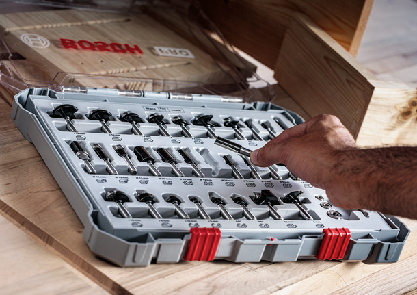 Seseorang memilih mata bor dari set yang tertata rapi di atas meja kayu.